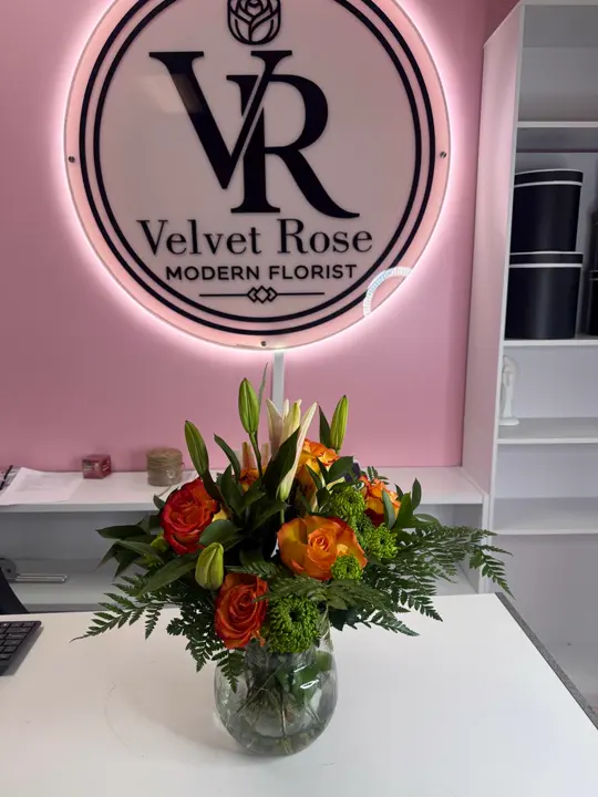 Orange roses and lilies arranged below the Velvet Rose sign